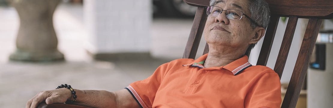 Elderly Asian man sits on a porch. 